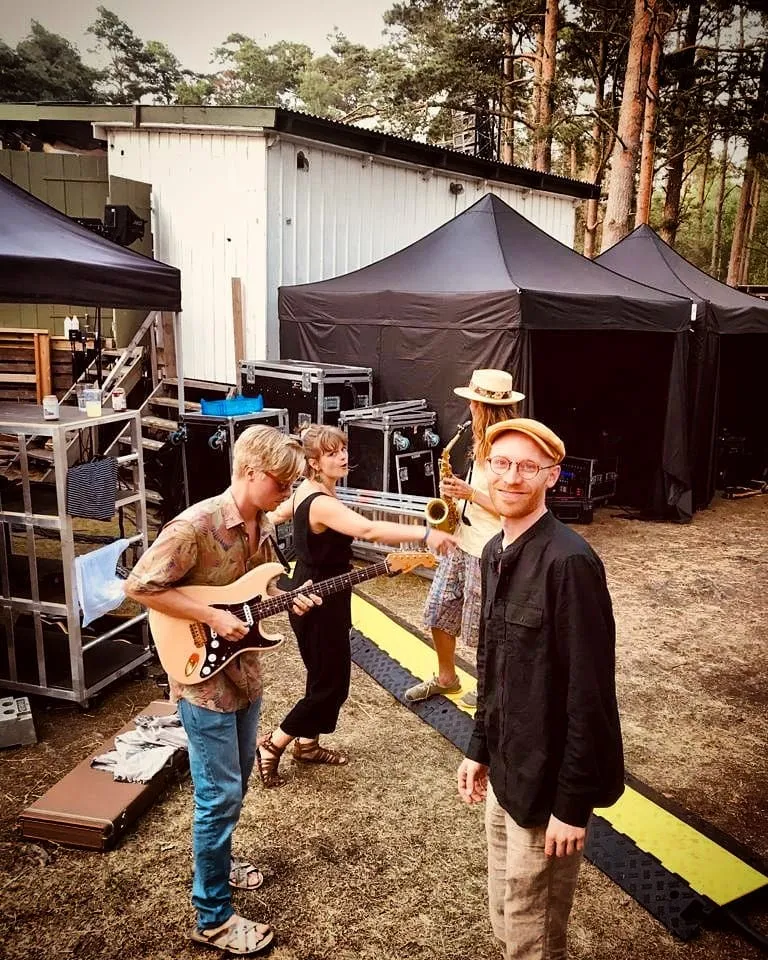 Backstage bland tält och flightcase, med gitarr och saxofon.